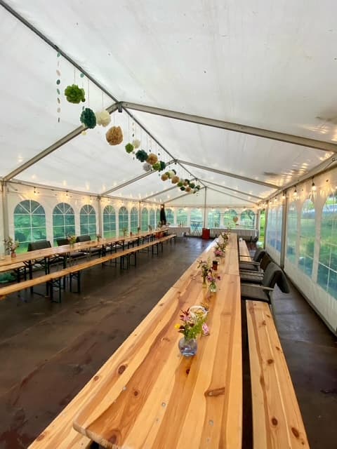 Smuk bordopsætning med træbænke og blomster i partytelt